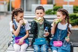Children sitting on a bench, eating from their lunchboxes.
