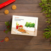 The Smart Garden 3 / Package with garden inside titled 'Growing plants, made easy' on a wooden surface with plants and cookies.